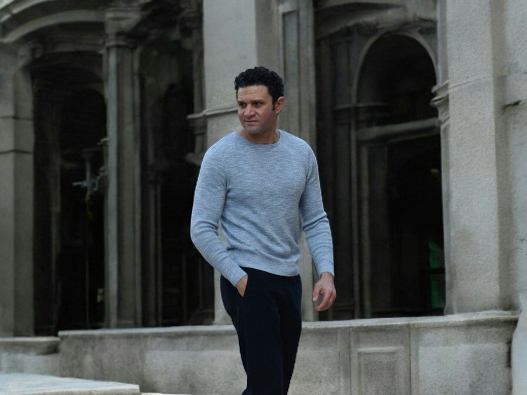 Man i grå stickad tröja och mörka byxor i en stenarkad